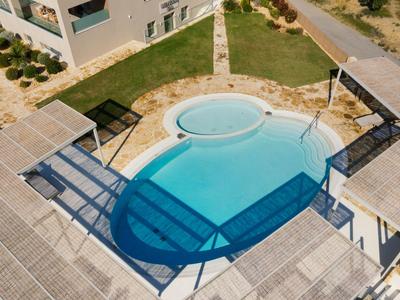 Vista aerea di una piscina ovale moderna con lastre di cemento circostanti e aree verdi.