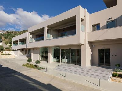 Moderní hotelový komplex s terasami a velkými skleněnými okny pod modrou oblohou.