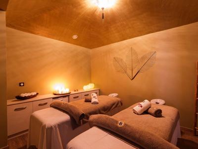 Příjemná masážní místnost se dvěma lůžky, teplým osvětlením a uklidňující atmosférou.