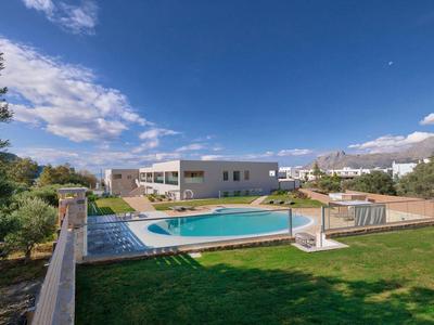 Moderní hotelový komplex s bazénem a zeleným trávníkem pod modrou oblohou.