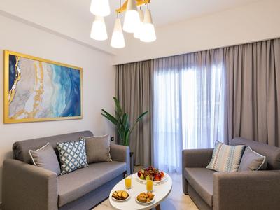 Moderně zařízený hotelový pokoj s dvěma pohovkami, stolem a velkým oknem s záclonami.