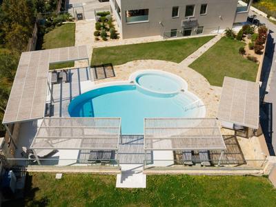 Piscina moderna con tettoia e lettini accanto a un edificio bianco