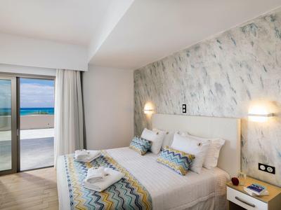 Světlo hotelový pokoj s manželskou postelí, moderními nástěnnými lampami a balkonem s výhledem na moře.