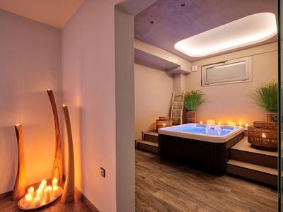 Příjemná wellness zóna s vířivkou, svíčkami a dřevěnou podlahou v hotelovém pokoji.