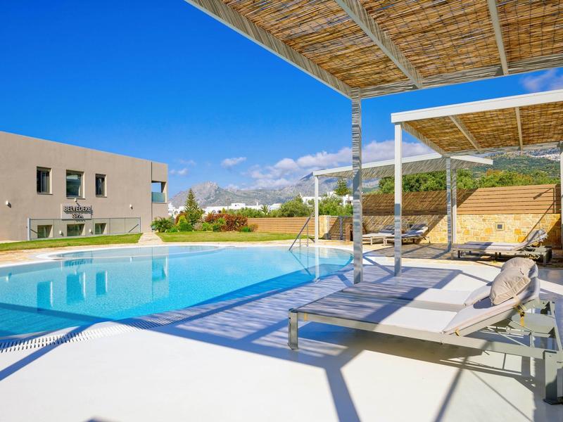 Moderní bazénová plocha s lehátky a stínem pod modrou oblohou.