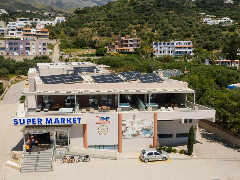 Budova supermarketu s solárními panely na střeše a zelenými kopci v pozadí.