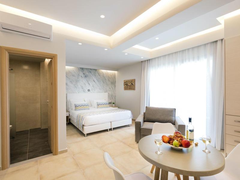 Světý hotelový pokoj s pohodlnou postelí, posezením a jídelním stolem s miskou ovoce.