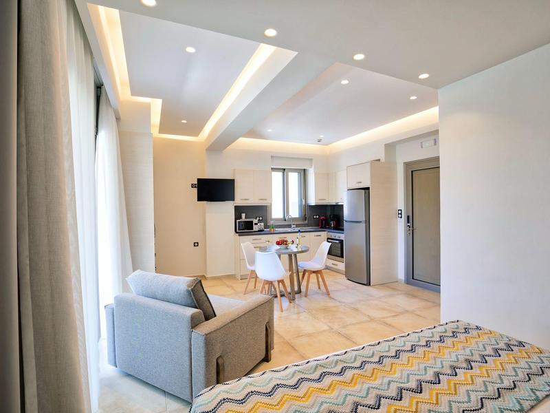 Moderně zařízený hotelový pokoj s postelí, pohovkou, jídelním stolem a kuchyňským koutem.