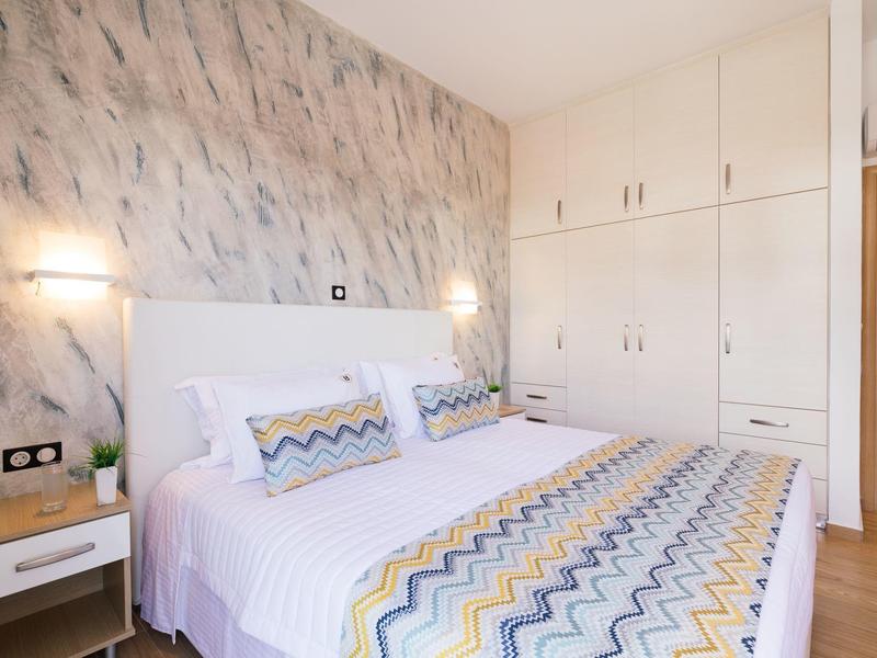 Světlá ložnice s manželskou postelí a velkými vestavěnými skříněmi v moderním stylu.