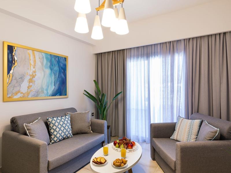 Moderně zařízený hotelový pokoj s dvěma pohovkami, stolem a velkým oknem s záclonami.