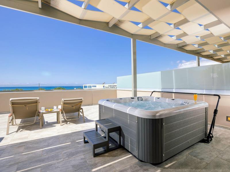 Střešní terasa s vířivkou, dvěma lehátky a výhledem na moře pod modrou oblohou.