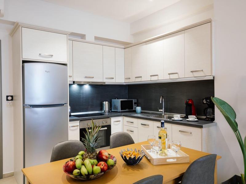 Moderní kuchyň s bílými skříňkami, nerezovou lednicí a jídelním stolem s ovocem a vínem.