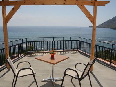 Deux chaises et une table sur une terrasse avec vue sur la mer et des poutres en bois.