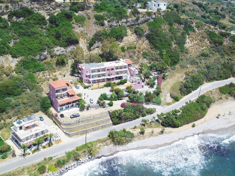 Meerdere huizen op een beboste helling boven een strand met heldere golven.