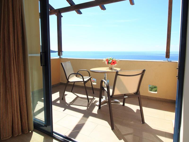 Balkon met twee stoelen en kleine tafel met uitzicht op zee bij heldere lucht.