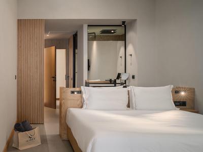 Modernes Hotelzimmer mit Doppelbett, hellen Wänden und offenem Badezimmer.