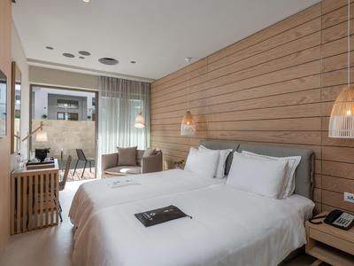Modernes Hotelzimmer mit zwei weißen Betten, Holzwand und Zugang zu Balkon mit Meerblick.