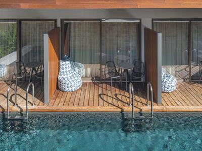 Außenansicht eines Hotels mit Holzterrasse und Pool, Stühle und Tische sichtbar.