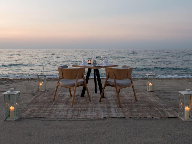 Romantyczny stół na plaży o zachodzie słońca z dwoma krzesłami i latarniami.