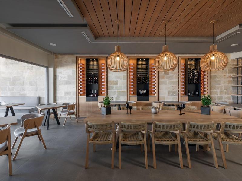 Nowoczesna jadalnia z drewnianymi meblami, stojakami na wino i dużymi oknami wpuszczającymi dużo światła.
