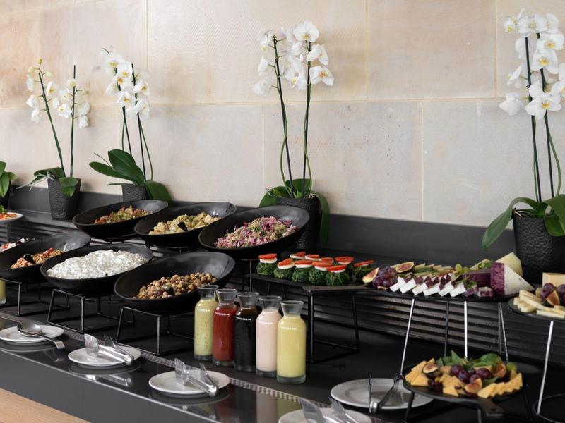 Bufet z różnorodnymi potrawami i białymi storczykami w tle.