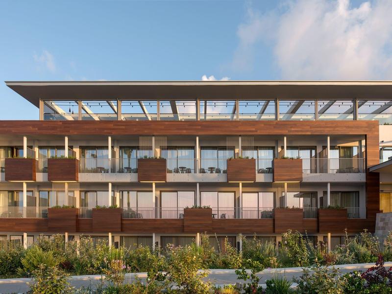 Nowoczesny budynek hotelu z drewnianą elewacją i dużymi szklanymi oknami w świetle dziennym.