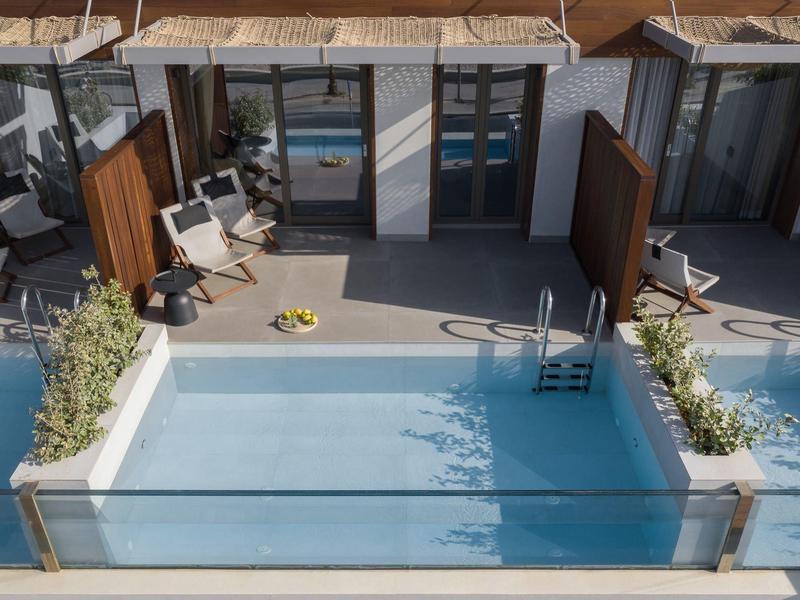 Dziedziniec z małym basenem, leżakami i szklanymi drzwiami do pokoi hotelowych.