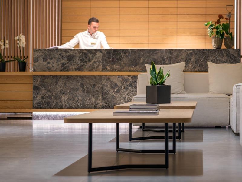 Nowoczesna lobby hotelowa z recepcją i miejscem do siedzenia, ozdobiona roślinami.