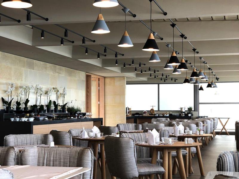 Nowoczesna, jasna restauracja z wieloma stołami i krzesłami, miękkie oświetlenie.