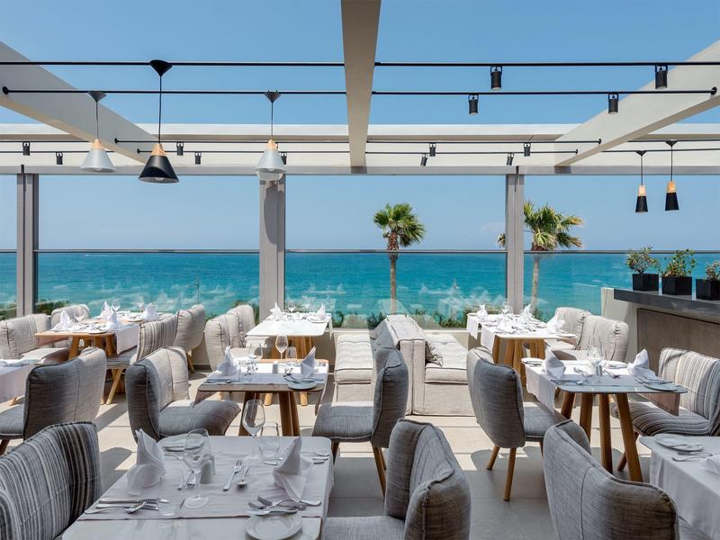 Elegancka restauracja z widokiem na morze i palmy pod bezchmurnym niebem.