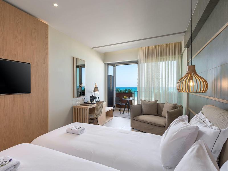 Nowoczesny pokój hotelowy z podwójnym łóżkiem, częścią wypoczynkową i widokiem na morze.