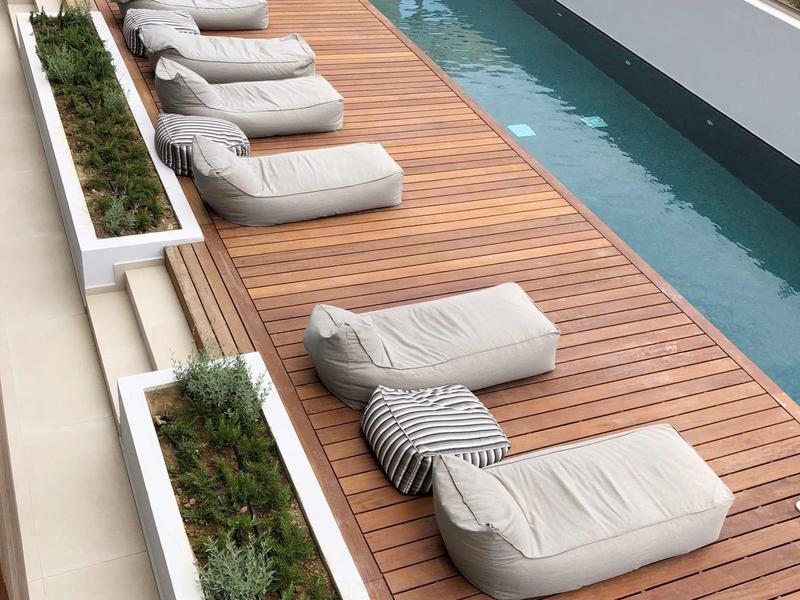 Nowoczesny drewniany taras z wygodnymi tapicerowanymi leżakami obok basenu.