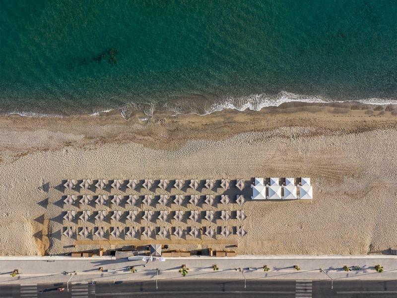 Widok z lotu ptaka na plażę z rzędami parasoli i leżaków przy wodzie.