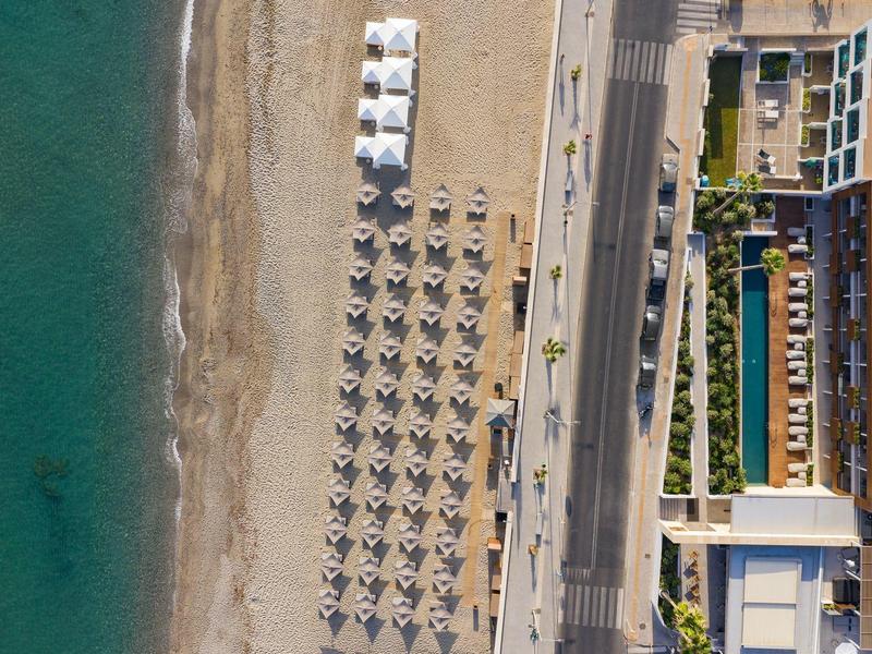 Widok z lotu ptaka na plażę z uporządkowanymi parasolami obok hotelu nad morzem.