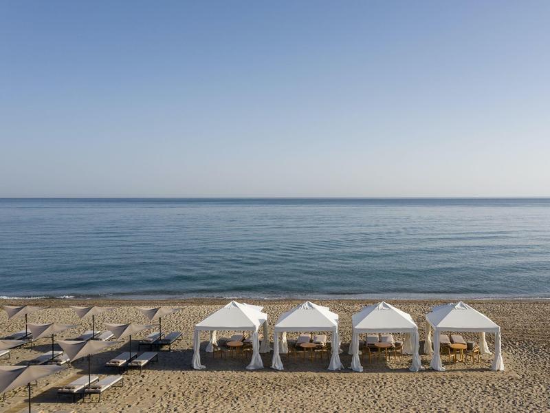 Cztery białe pawilony na spokojnej piaszczystej plaży z widokiem na niebieskie morze.