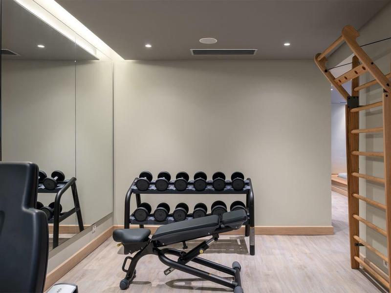 Nowoczesna siłownia z hantlami, ławką treningową i ścianką wspinaczkową.