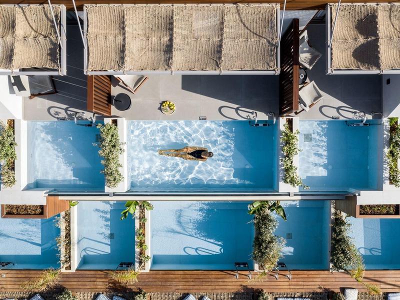 Widok z lotu ptaka na basen z leżakami i zacienionymi miejscami w kompleksie hotelowym.