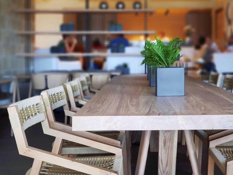 Nowoczesna jadalnia z drewnianym stołem, plecionymi krzesłami i roślinami doniczkowymi w restauracji hotelowej.