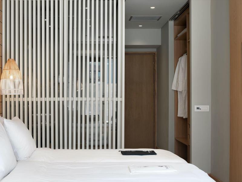 Nowoczesny pokój hotelowy z białym łóżkiem, drewnianymi akcentami i ścianką działową.