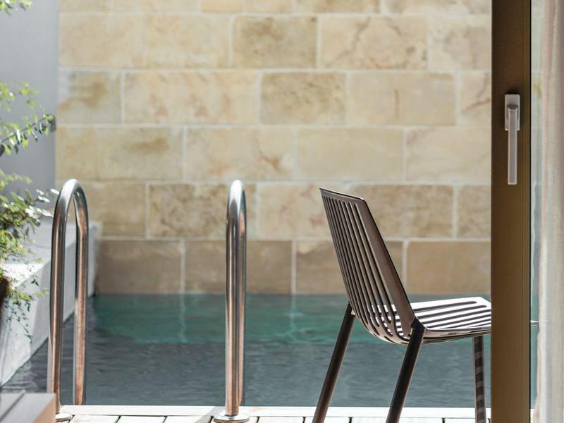 Nowoczesne drewniane krzesło na tarasie obok basenu z jasnym kamiennym murem.