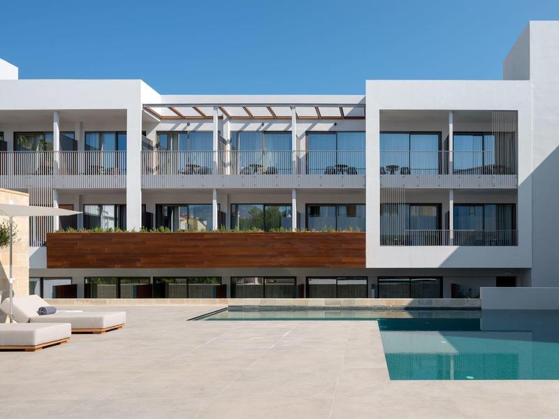 Nowoczesny kompleks hotelowy z basenem, tarasem słonecznym i białymi budynkami pod niebieskim niebem.