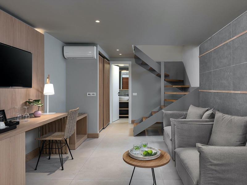 Nowoczesny hol hotelowy z szarą sofą, drewnianym biurkiem i schodami w tle.