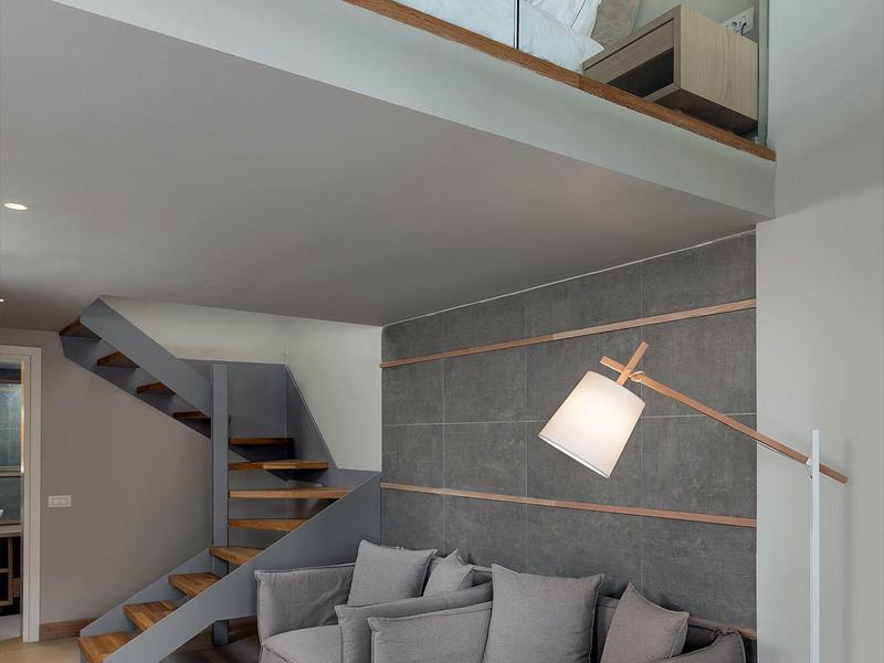 Nowoczesny salon z szarą sofą narożną, lampą stojącą i schodami na piętro.