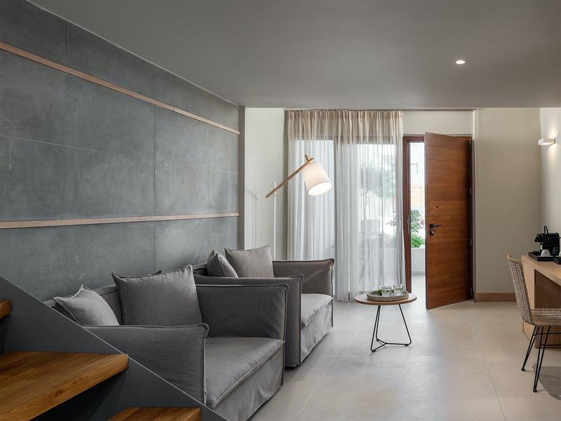 Nowoczesna część pokoju hotelowego z szarymi fotelami, drewnianymi meblami i otwartymi drewnianymi drzwiami.