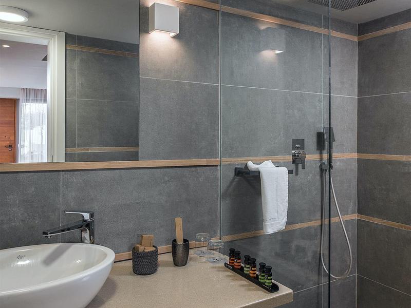 Nowoczesny prysznic hotelowy ze szklaną ścianką i umywalką na drewnianej półce, szare płytki ścienne.