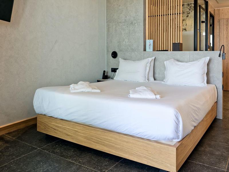 Nowoczesny pokój dwuosobowy z drewnianym łóżkiem, białą pościelą i telewizorem ściennym.