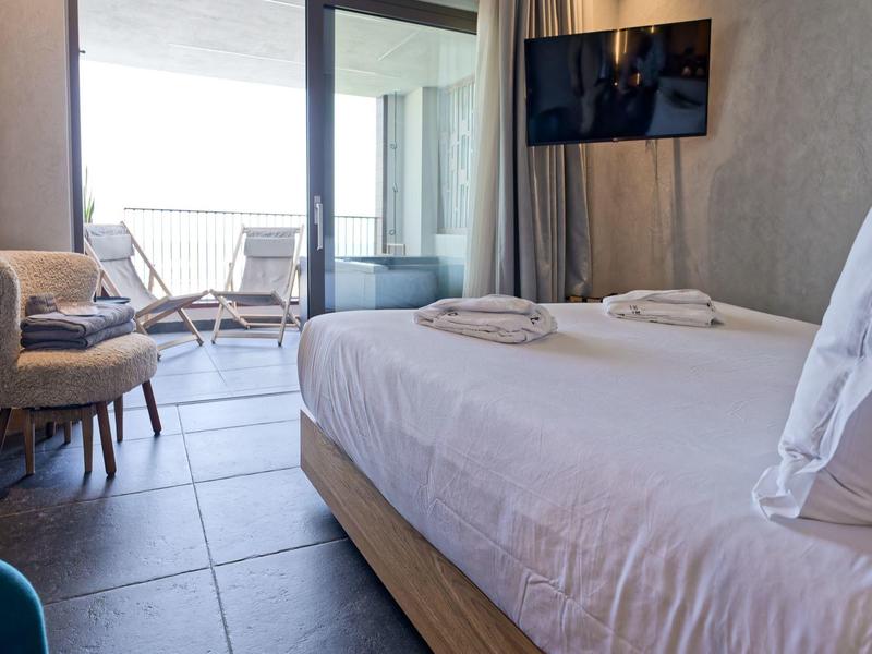 Nowoczesny pokój hotelowy z podwójnym łóżkiem, krzesłami i balkonem z miejscem do siedzenia.