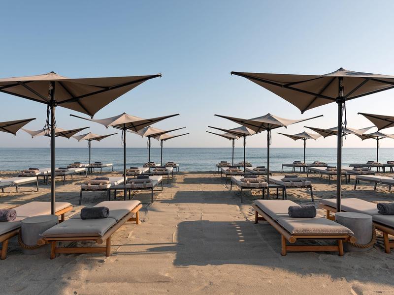 Puste leżaki z parasolami na spokojnej, słonecznej, piaszczystej plaży z widokiem na morze.