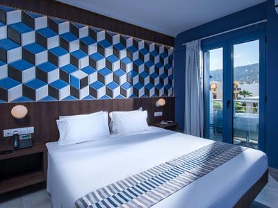 Camera d'hotel moderna con letto grande, parete con motivo geometrico e balcone con vista esterna.