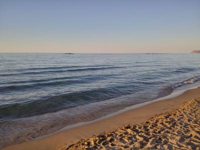 Tramonto su mare calmo con spiaggia sabbiosa in primo piano.